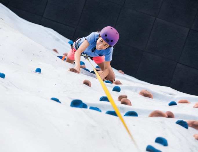 A woman climbing up the side of an artificial rock wall.