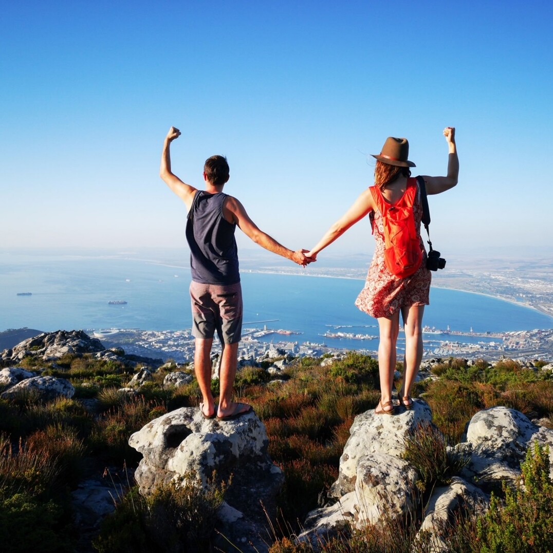 Two people standing on top of a hill holding hands.