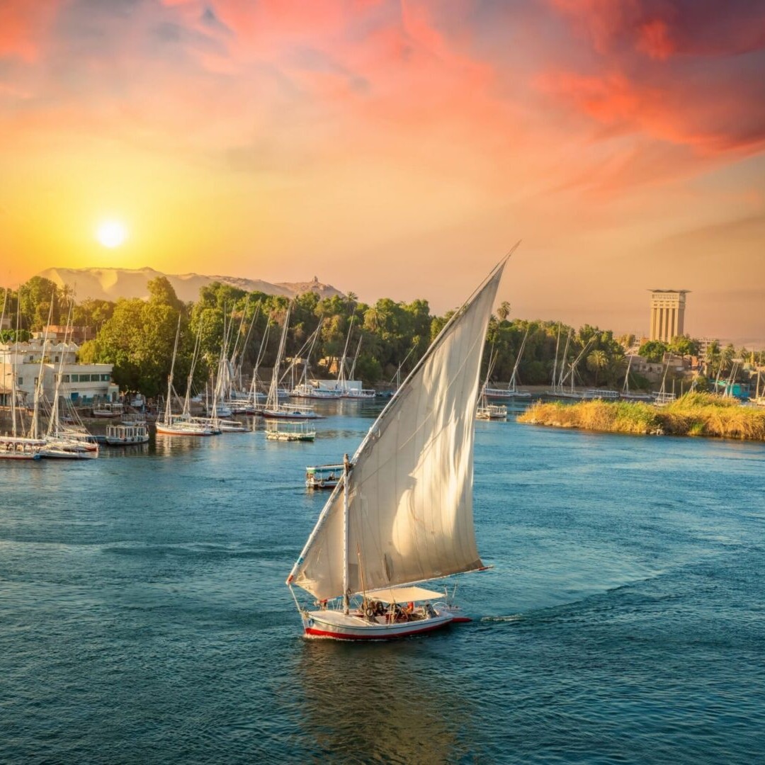 A sailboat is sailing in the water at sunset.