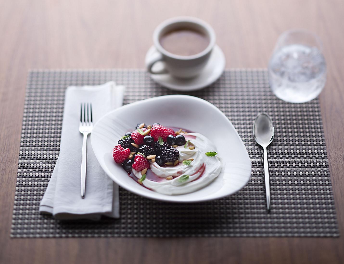 A bowl of yogurt with berries and nuts on the side.