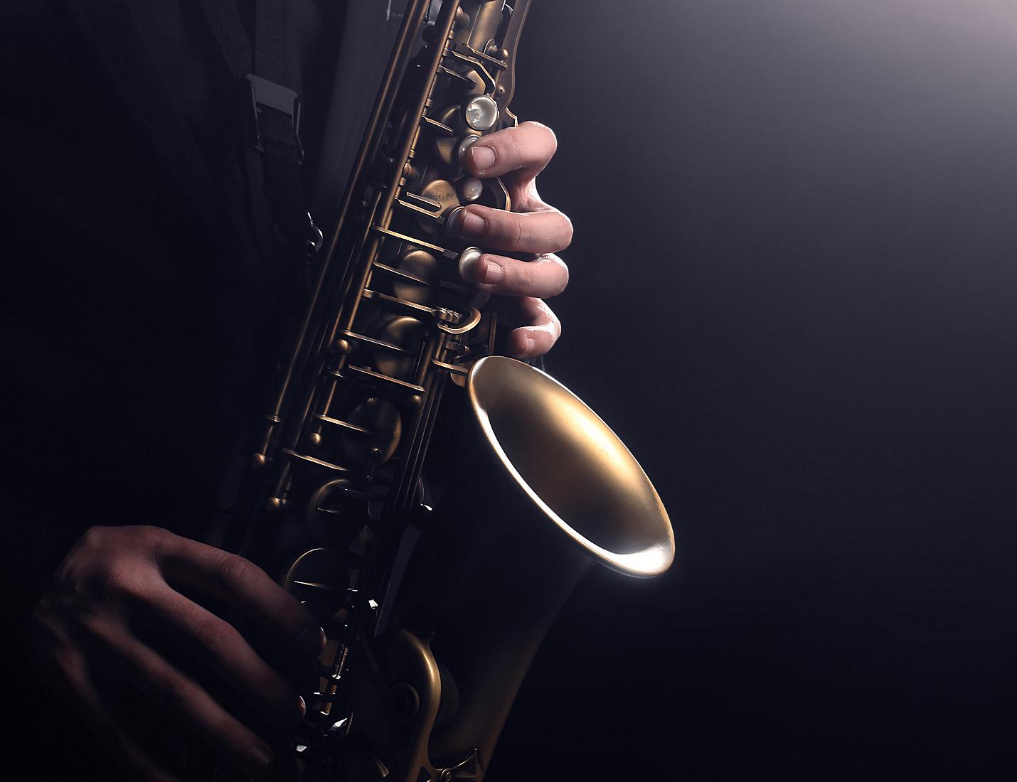 A person playing the saxophone in front of a dark background.